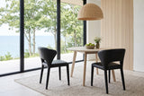 Two Petralia dining chairs in Black leather seen from behind at a round white-oak table in a Bayfield bluff house