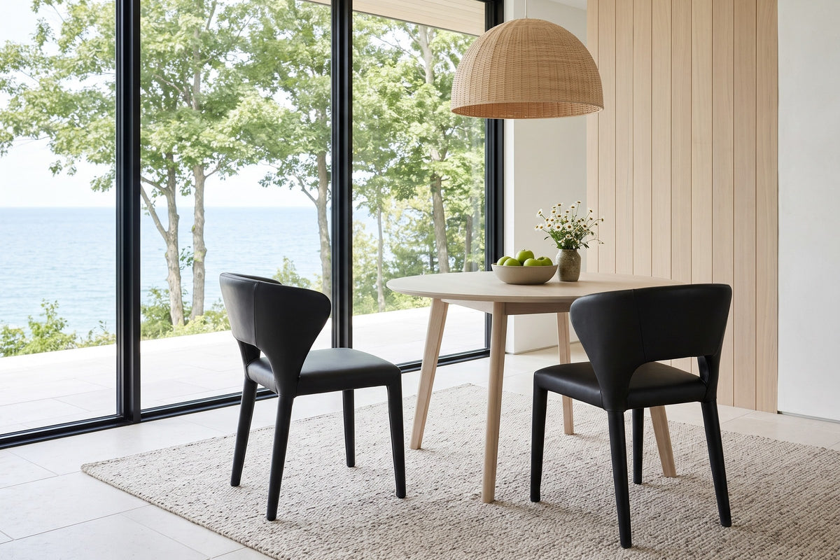 Two Petralia dining chairs in Black leather seen from behind at a round white-oak table in a Bayfield bluff house