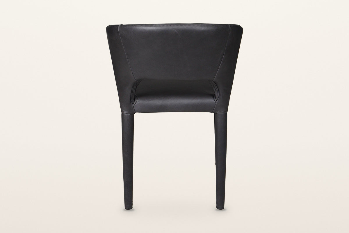 Back of the Petralia dining chair in Black leather on a warm white studio backdrop: a smooth wrapped shell with a low slot ab