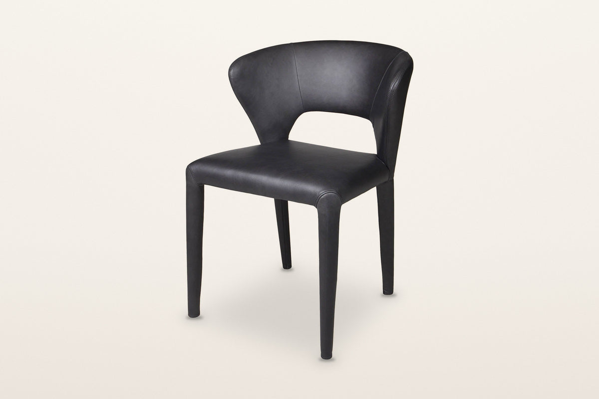 Petralia dining chair in Black leather, three-quarter view on a warm white studio backdrop