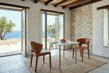 Two Petralia dining chairs in Brown leather across a small marble table in a Hydra island house