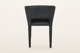 Back of the Petralia dining chair in Dark Grey on a warm white studio backdrop: a smooth wrapped shell with a low slot above