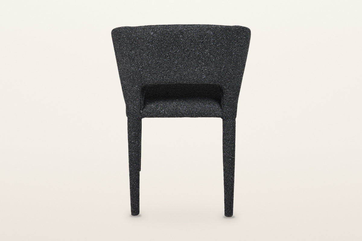 Back of the Petralia dining chair in Dark Grey on a warm white studio backdrop: a smooth wrapped shell with a low slot above