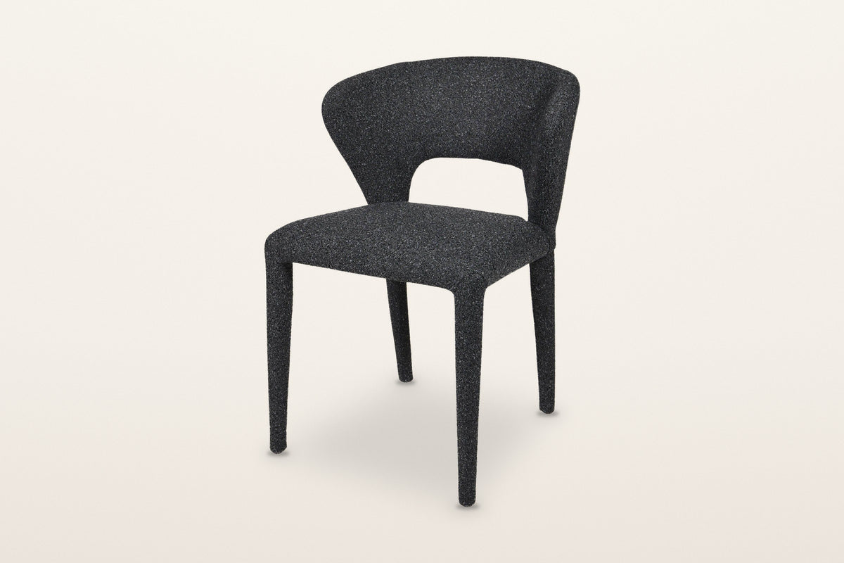 Petralia dining chair in Dark Grey, three-quarter view on a warm white studio backdrop: a curved back that wraps around the s