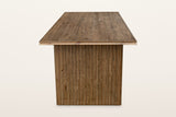 End view of the Pettorano dining table in Brown on a warm white studio backdrop: the reeded outer face of a slab leg under th
