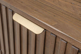 Close-up of a Pettorano brass lip pull folded over the top edge of a reeded drawer front, under the planked top