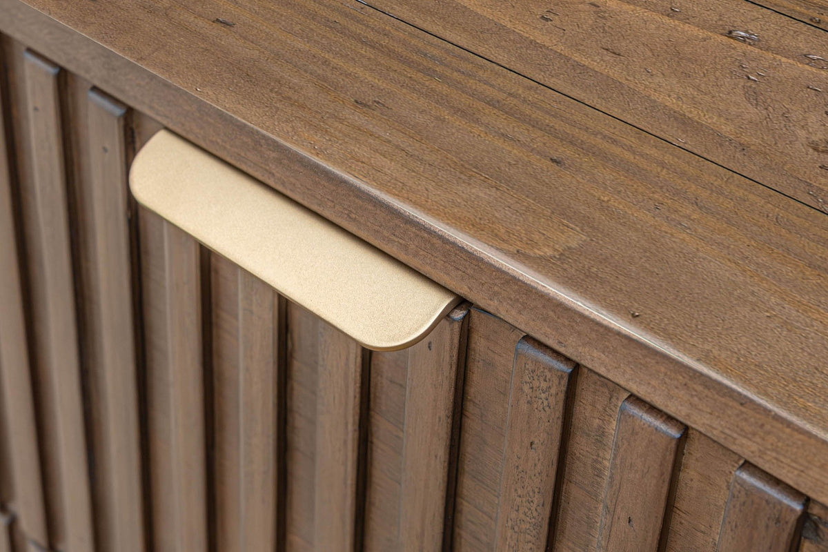 Close-up of a Pettorano brass lip pull folded over the top edge of a reeded drawer front, under the planked top