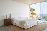 Pettorano nightstand in Brown left of a white linen bed in a Sagres cliff house bedroom, with white lime plaster