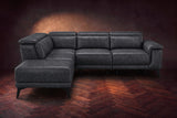 The Pista sectional in Aged Slate distressed full leather on a dark walnut herringbone floor against a brown plaster wall, seen from the front with the chaise toward the camera, headrests down and footrest closed. Shown in Aged Slate, Left chaise.