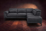 The Pista sectional in Aged Slate distressed full leather on a dark walnut herringbone floor against a brown plaster wall, seen from the front with the chaise toward the camera, headrests down and footrest closed. Shown in Aged Slate, Right chaise.