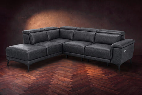 The Pista sectional in Aged Slate distressed full leather on a dark walnut herringbone floor against a brown plaster wall, three-quarter view from the arm end, headrests down and footrest closed. Shown in Aged Slate, Left chaise.