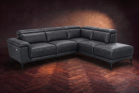 The Pista sectional in Aged Slate distressed full leather on a dark walnut herringbone floor against a brown plaster wall, three-quarter view from the arm end, headrests down and footrest closed. Shown in Aged Slate, Right chaise.