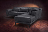 The Pista sectional in Aged Slate distressed full leather on a dark walnut herringbone floor against a brown plaster wall, seen from the chaise end, headrests down and footrest closed. Shown in Aged Slate, Right chaise.