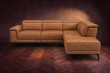 The Pista sectional in Antiqued Caramel distressed full leather on a dark walnut herringbone floor against a brown plaster wall, seen from the front with the chaise toward the camera, headrests down and footrest closed. Shown in Antiqued Caramel, Right chaise.