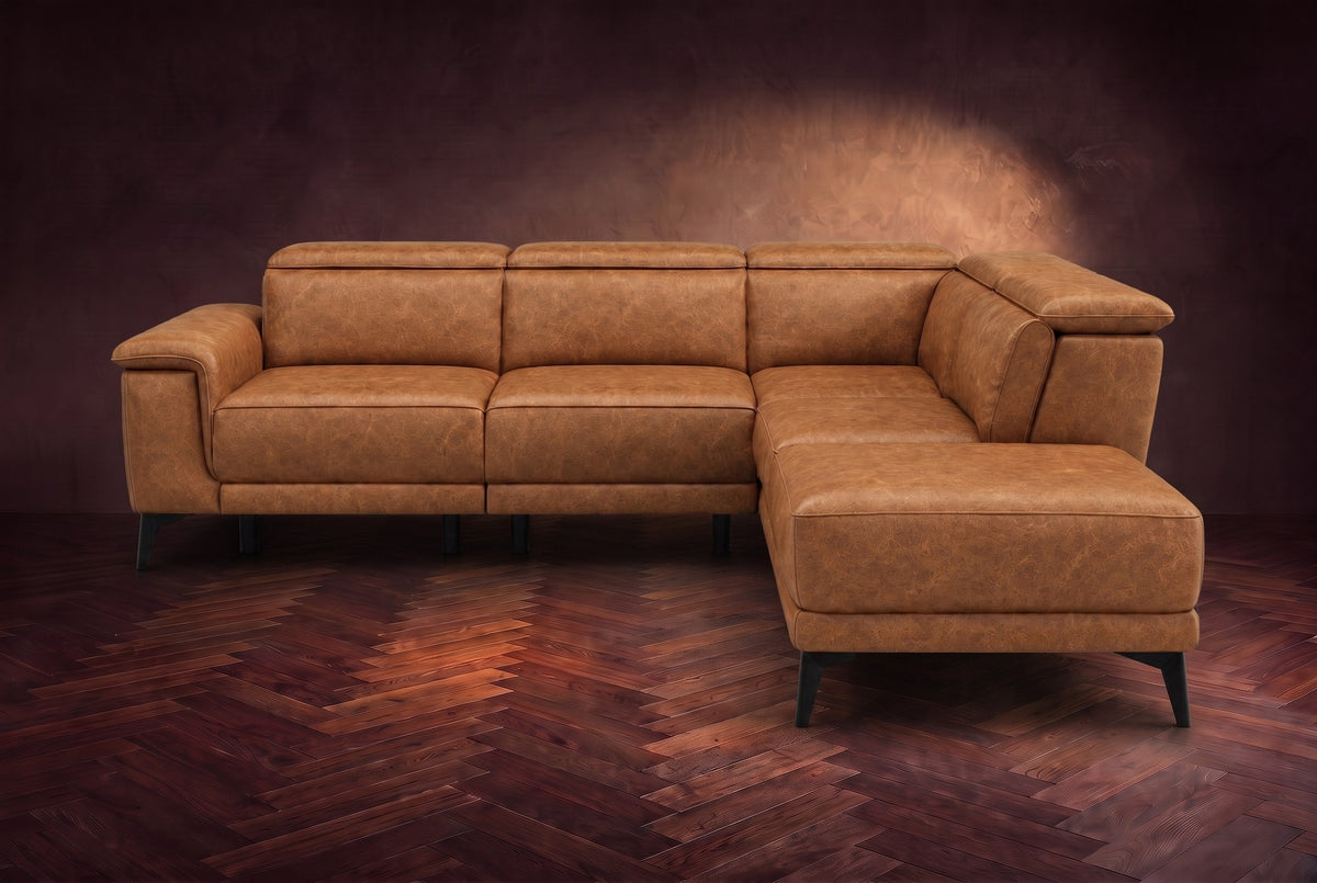 The Pista sectional in Antiqued Caramel distressed full leather on a dark walnut herringbone floor against a brown plaster wall, seen from the front with the chaise toward the camera, headrests down and footrest closed. Shown in Antiqued Caramel, Right chaise.