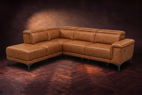 The Pista sectional in Antiqued Caramel distressed full leather on a dark walnut herringbone floor against a brown plaster wall, three-quarter view from the arm end, headrests down and footrest closed. Shown in Antiqued Caramel, Left chaise.