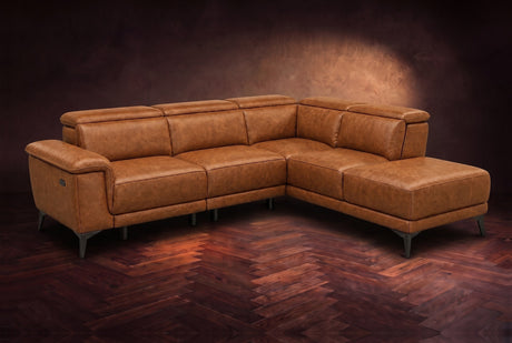 The Pista sectional in Antiqued Caramel distressed full leather on a dark walnut herringbone floor against a brown plaster wall, three-quarter view from the arm end, headrests down and footrest closed. Shown in Antiqued Caramel, Right chaise.