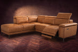 The Pista sectional in Antiqued Caramel distressed full leather on a dark walnut herringbone floor against a brown plaster wall, the seat beside the box arm reclined with its two-tier footrest out and its headrest raised, the other headrests down. Shown in Antiqued Caramel, Left chaise.