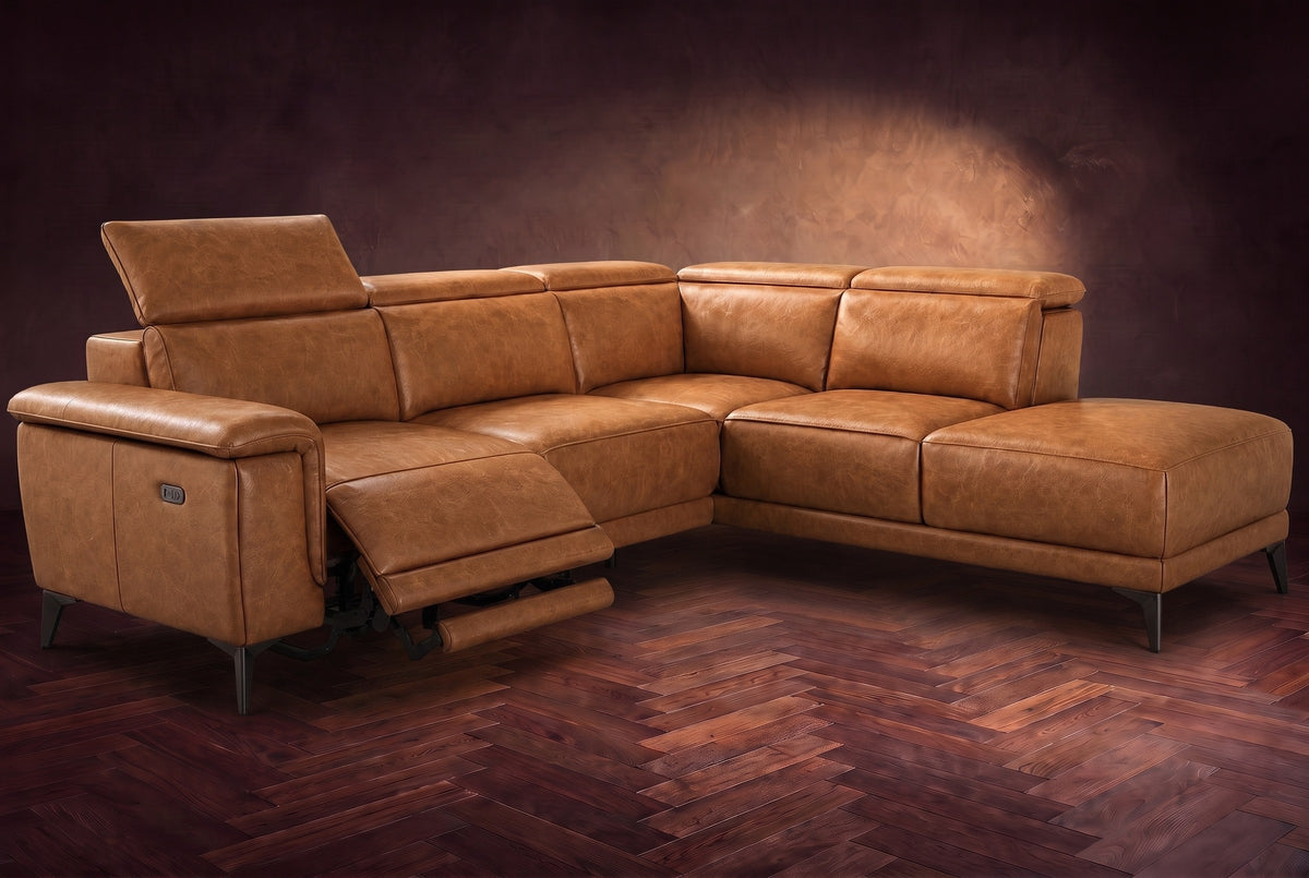 The Pista sectional in Antiqued Caramel distressed full leather on a dark walnut herringbone floor against a brown plaster wall, the seat beside the box arm reclined with its two-tier footrest out and its headrest raised, the other headrests down. Shown in Antiqued Caramel, Right chaise.