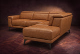 The Pista sectional in Antiqued Caramel distressed full leather on a dark walnut herringbone floor against a brown plaster wall, seen from the chaise end, headrests down and footrest closed. Shown in Antiqued Caramel, Right chaise.