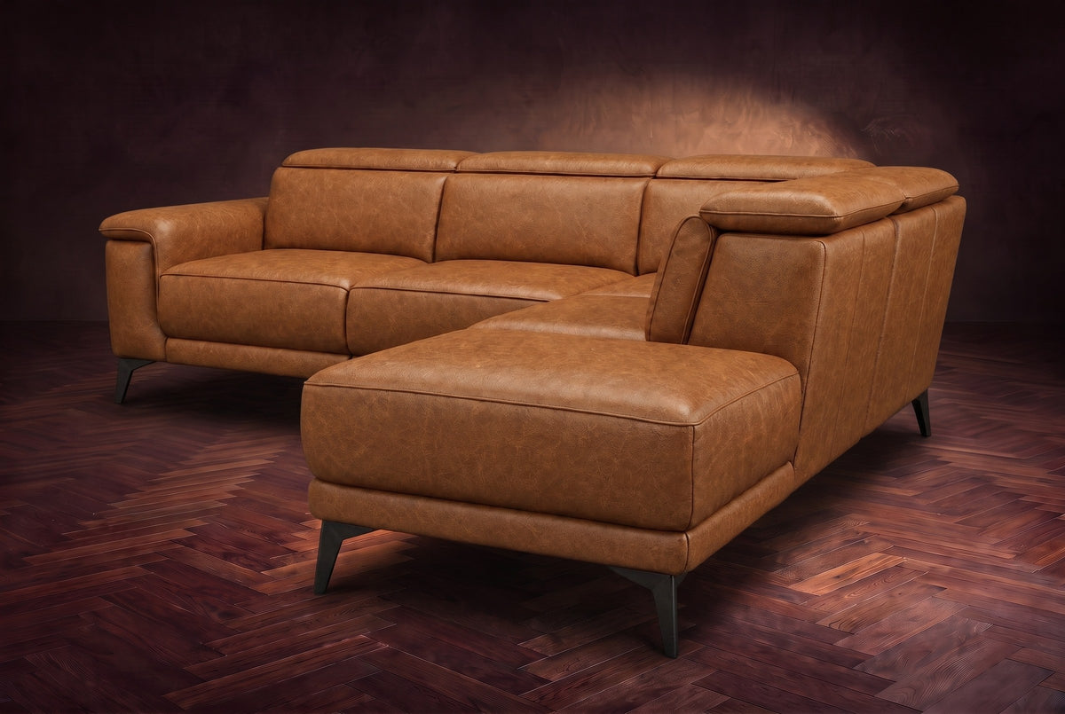 The Pista sectional in Antiqued Caramel distressed full leather on a dark walnut herringbone floor against a brown plaster wall, seen from the chaise end, headrests down and footrest closed. Shown in Antiqued Caramel, Right chaise.