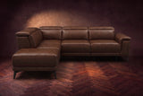 The Pista sectional in Burnished Chestnut distressed full leather on a dark walnut herringbone floor against a brown plaster wall, seen from the front with the chaise toward the camera, headrests down and footrest closed. Shown in Burnished Chestnut, Left chaise.
