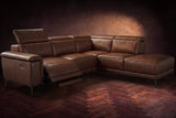 The Pista sectional in Burnished Chestnut distressed full leather on a dark walnut herringbone floor against a brown plaster wall, the seat beside the box arm reclined with its two-tier footrest out and its headrest raised, the other headrests down. Shown in Burnished Chestnut, Right chaise.