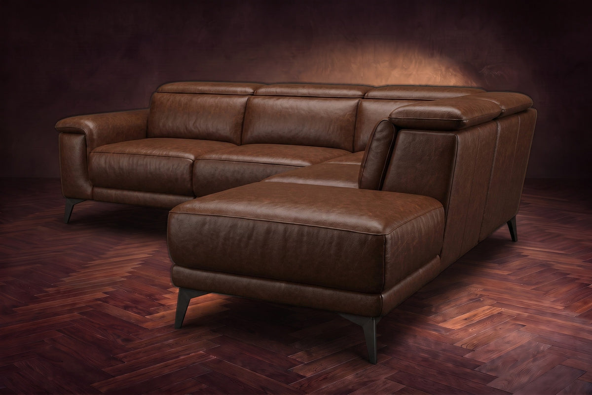 The Pista sectional in Burnished Chestnut distressed full leather on a dark walnut herringbone floor against a brown plaster wall, seen from the chaise end, headrests down and footrest closed. Shown in Burnished Chestnut, Right chaise.
