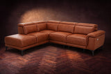The Pista sectional in Tuscan Cognac distressed full leather on a dark walnut herringbone floor against a brown plaster wall, three-quarter view from the arm end, headrests down and footrest closed. Shown in Tuscan Cognac, Left chaise.