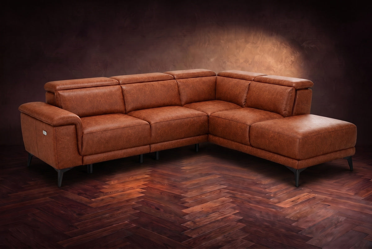 The Pista sectional in Tuscan Cognac distressed full leather on a dark walnut herringbone floor against a brown plaster wall, three-quarter view from the arm end, headrests down and footrest closed. Shown in Tuscan Cognac, Right chaise.