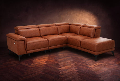 The Pista sectional in Tuscan Cognac distressed full leather on a dark walnut herringbone floor against a brown plaster wall, three-quarter view from the arm end, headrests down and footrest closed. Shown in Tuscan Cognac, Right chaise.