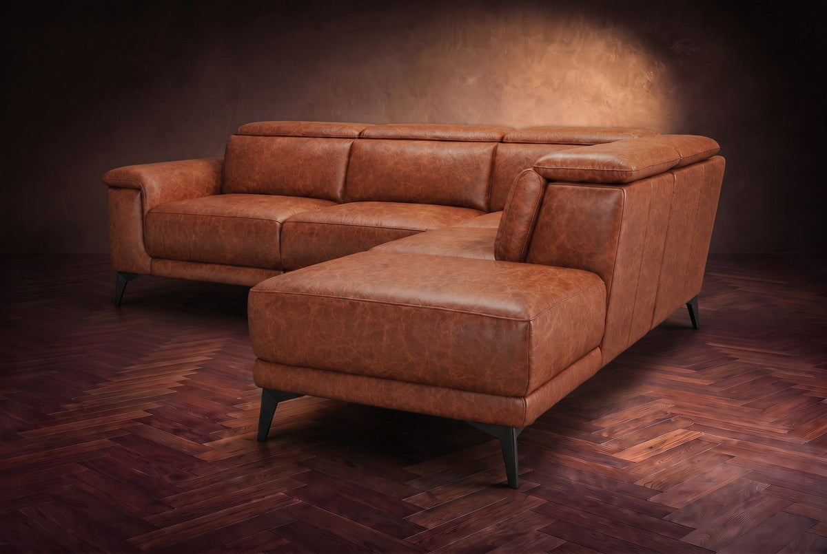 The Pista sectional in Tuscan Cognac distressed full leather on a dark walnut herringbone floor against a brown plaster wall, seen from the chaise end, headrests down and footrest closed. Shown in Tuscan Cognac, Right chaise.