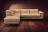 The Pista sectional in Washed Sand distressed full leather on a dark walnut herringbone floor against a brown plaster wall, seen from the front with the chaise toward the camera, headrests down and footrest closed. Shown in Washed Sand, Left chaise.