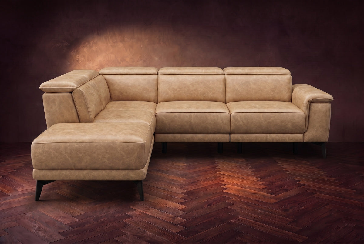 The Pista sectional in Washed Sand distressed full leather on a dark walnut herringbone floor against a brown plaster wall, seen from the front with the chaise toward the camera, headrests down and footrest closed. Shown in Washed Sand, Left chaise.