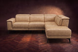 The Pista sectional in Washed Sand distressed full leather on a dark walnut herringbone floor against a brown plaster wall, seen from the front with the chaise toward the camera, headrests down and footrest closed. Shown in Washed Sand, Right chaise.