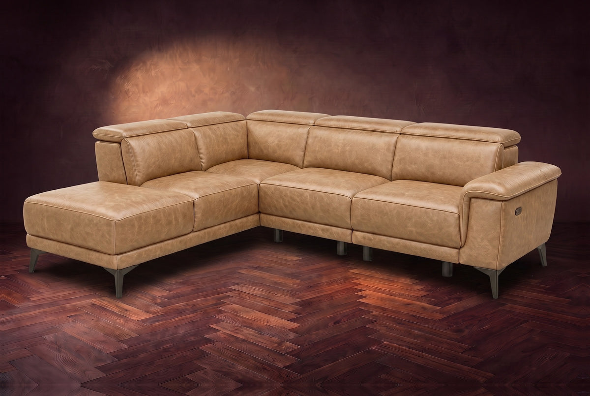 The Pista sectional in Washed Sand distressed full leather on a dark walnut herringbone floor against a brown plaster wall, three-quarter view from the arm end, headrests down and footrest closed. Shown in Washed Sand, Left chaise.