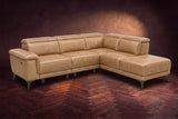 The Pista sectional in Washed Sand distressed full leather on a dark walnut herringbone floor against a brown plaster wall, three-quarter view from the arm end, headrests down and footrest closed. Shown in Washed Sand, Right chaise.