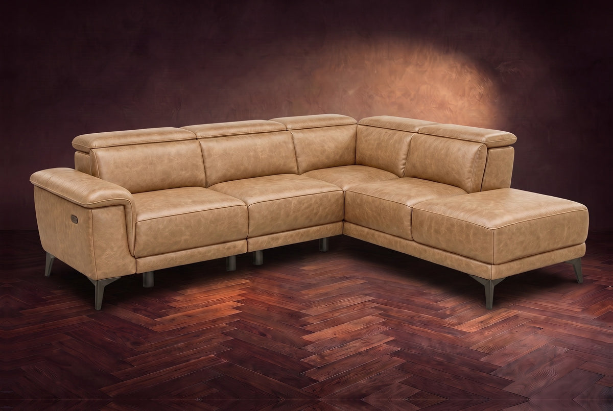 The Pista sectional in Washed Sand distressed full leather on a dark walnut herringbone floor against a brown plaster wall, three-quarter view from the arm end, headrests down and footrest closed. Shown in Washed Sand, Right chaise.