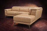 The Pista sectional in Washed Sand distressed full leather on a dark walnut herringbone floor against a brown plaster wall, seen from the chaise end, headrests down and footrest closed. Shown in Washed Sand, Right chaise.