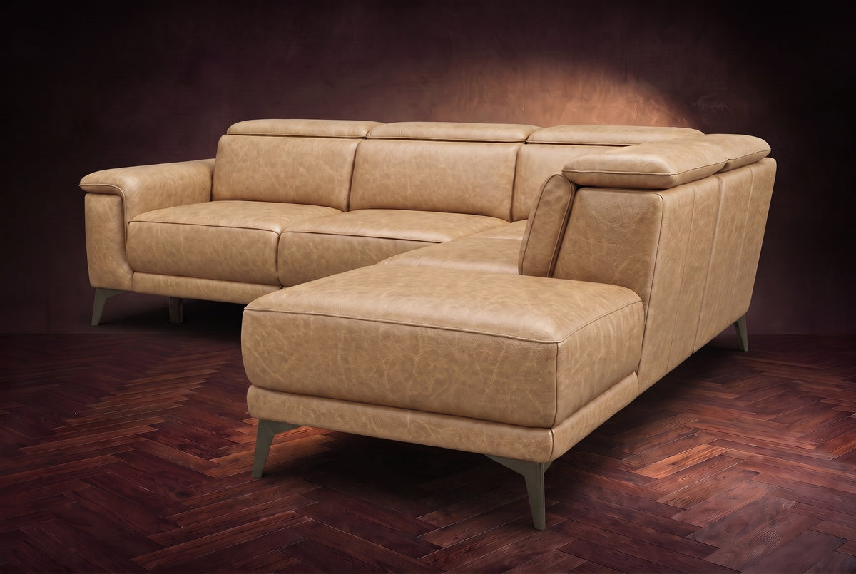 The Pista sectional in Washed Sand distressed full leather on a dark walnut herringbone floor against a brown plaster wall, seen from the chaise end, headrests down and footrest closed. Shown in Washed Sand, Right chaise.