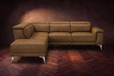 The Pista sectional in Weathered Saddle distressed full leather on a dark walnut herringbone floor against a brown plaster wall, seen from the front with the chaise toward the camera, headrests down and footrest closed. Shown in Weathered Saddle, Left chaise.