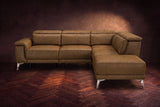 The Pista sectional in Weathered Saddle distressed full leather on a dark walnut herringbone floor against a brown plaster wall, seen from the front with the chaise toward the camera, headrests down and footrest closed. Shown in Weathered Saddle, Right chaise.