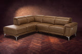 The Pista sectional in Weathered Saddle distressed full leather on a dark walnut herringbone floor against a brown plaster wall, three-quarter view from the arm end, headrests down and footrest closed. Shown in Weathered Saddle, Left chaise.