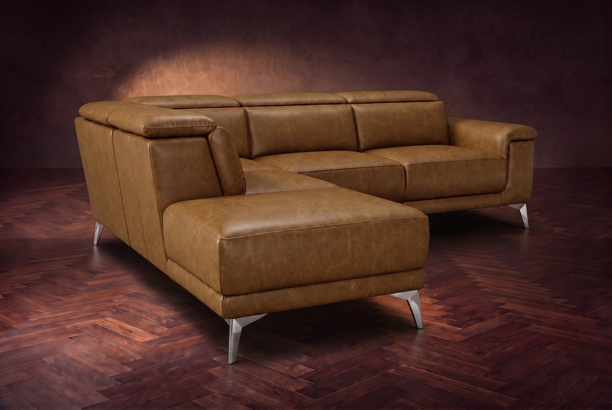 The Pista sectional in Weathered Saddle distressed full leather on a dark walnut herringbone floor against a brown plaster wall, seen from the chaise end, headrests down and footrest closed. Shown in Weathered Saddle, Left chaise.