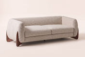 Pistoia boucle sofa in almond on four walnut-finish wooden wedge feet, three-quarter view on a warm off-white studio backdrop