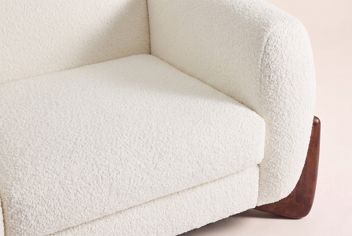 Close-up of the Beige boucle seat cushion and the rounded arm above a walnut wedge foot