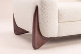 Close-up of the sculpted walnut wedge foot hugging the Beige boucle arm of the Pistoia sofa