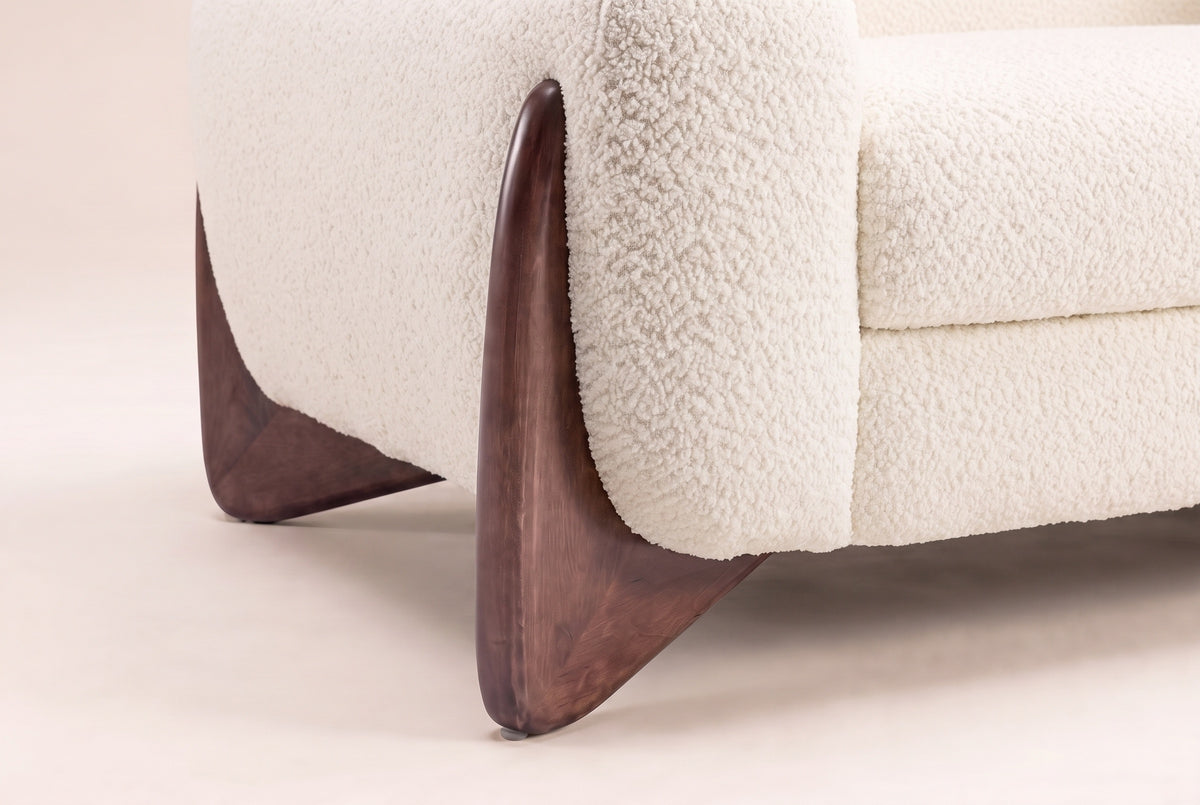 Close-up of the sculpted walnut wedge foot hugging the Beige boucle arm of the Pistoia sofa