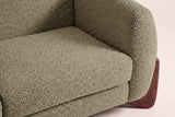 Close-up of the Olive Green boucle seat cushion and the rounded arm above a walnut wedge foot