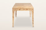 End view of the Polcenigo dining table in Honey Blonde Burl on a warm white studio backdrop: the curved knees where each leg
